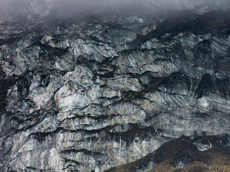Aerial view of a rugged glacier surface featuring deep crevasses layers of compressed ice and dark moraine debris in Nepal.