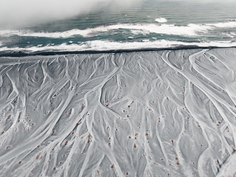 Aerial view of a braided river delta with intricate sediment patterns flowing across a dark volcanic sand beach into the North Atlantic Ocean in Iceland. Aerial view of a braided river delta with intricate sediment patterns flowing across a dark volcanic sand beach into the North Atlantic Ocean in Iceland.