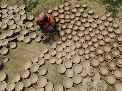 Joypurhat Bangladesh 28 September 2026 Aerial view of a woman crafting traditional clay pottery on the ground surrounded by numerous finished bowls drying under the sun. Joypurhat Bangladesh 28 September 2026 Aerial view of a woman crafting traditional clay pottery on the ground surrounded by numerous finished bowls drying under the sun.