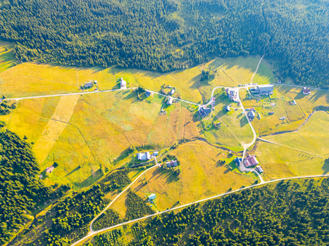 Aerial view of Jizerka village nestled among lush green meadows and dense pine forests with winding roads and small houses under warm golden hour light in Korenov Liberec Region Czechia. Aerial view of Jizerka village nestled among lush green meadows and dense pine forests with winding roads and small houses under warm golden hour light in Korenov Liberec Region Czechia.