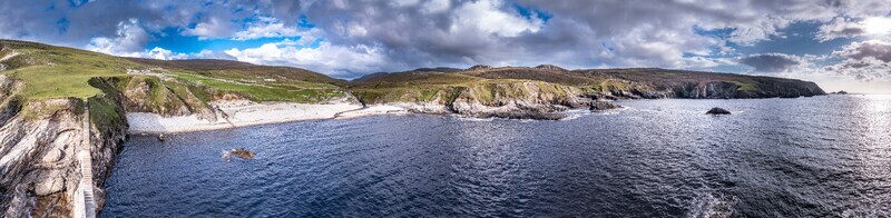 Aerial view of the rugged coastline and cliffs at An Port featuring a small beach green hills and dark ocean waters in Ardara County Donegal Ireland.