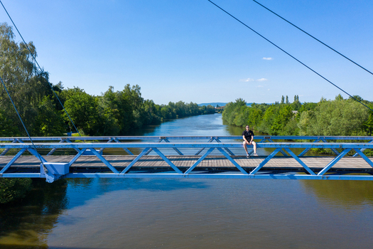 Aerial view of Sportinsel Forchheim Spazierweg und Spielplatz featuring a blue metal bridge over a river with a person sitting on the railing Forchheim Bayern Germany.
