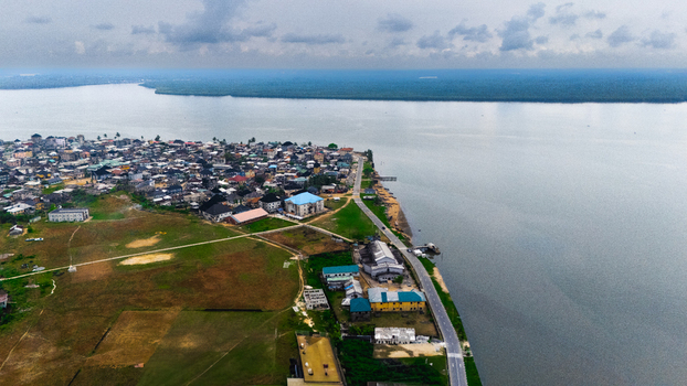 Aerial view of the coastal town with dense residential buildings a winding road along the shoreline and calm water under a cloudy sky in Minima Rivers Nigeria.