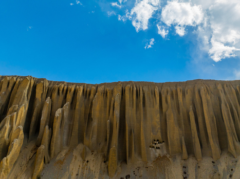 Aerial view of the dramatic vertically eroded cliff formations in the Mustang region featuring deep fluted ridges and sandy textures under a bright blue sky in Nepal.