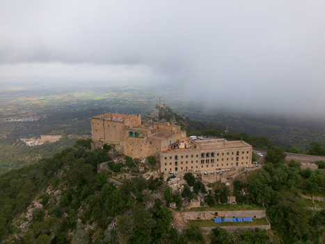 Aerial view of the Sanctuary of Sant Salvador on a rocky hilltop surrounded by lush green trees and low hanging clouds in Felanitx Illes Balears Spain. Aerial view of the Sanctuary of Sant Salvador on a rocky hilltop surrounded by lush green trees and low hanging clouds in Felanitx Illes Balears Spain.