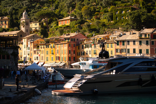 View of Portofino harbor with yachts moored at the pier and the historic church tower against lush green hills in Portofino Liguria Italy.