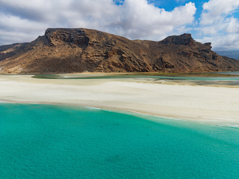 Aerial view of turquoise waters meeting pristine white sands beneath a rugged mountain range Detwah lagoon Socotra Yemen.