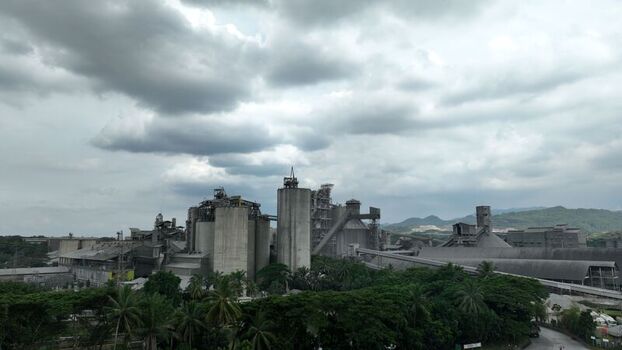 Aerial view of the industrial cement factory with large concrete silos conveyor systems and surrounding lush tropical forest under a cloudy sky in Klapanunggal West Java Indonesia. Aerial view of the industrial cement factory with large concrete silos conveyor systems and surrounding lush tropical forest under a cloudy sky in Klapanunggal West Java Indonesia.