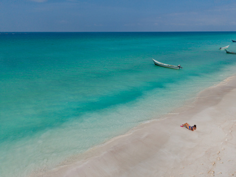 Aerial view of a tranquil beach with white sand meeting the turquoise sea where a lone figure reclines under the sun Shoab beach Socotra Yemen. Aerial view of a tranquil beach with white sand meeting the turquoise sea where a lone figure reclines under the sun Shoab beach Socotra Yemen.