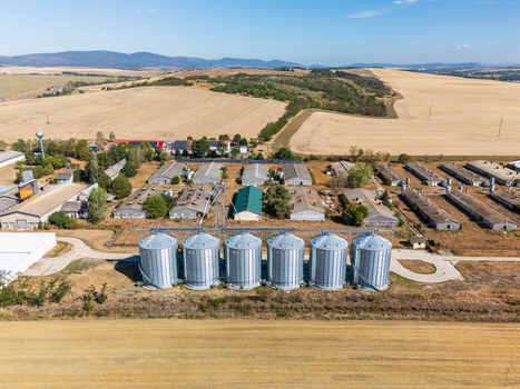 Aerial view of grain silos and feed mill facilities in Paszto Nograd County Northern Hungary surrounded by farmland wheat fields and rural hills in summer. Aerial view of grain silos and feed mill facilities in Paszto Nograd County Northern Hungary surrounded by farmland wheat fields and rural hills in summer.