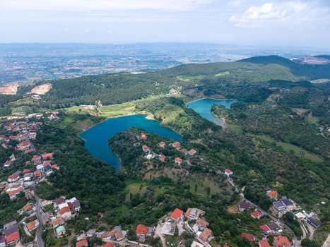 Aerial view of a vibrant blue lake surrounded by lush green hills and residential houses with red roofs in Kruje Durres County Albania.