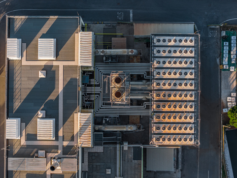 Aerial view of an industrial plant rooftop featuring rows of HVAC units complex piping systems and long shadows cast across the flat roof in Rome Lazio Italy.