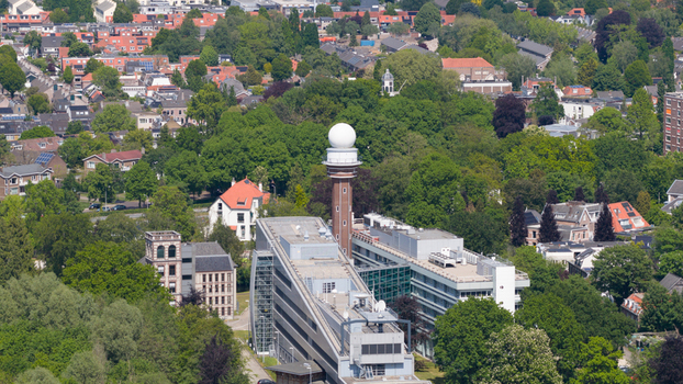 Aerial view of the KNMI building complex featuring its iconic radar tower and white dome surrounded by dense green trees and suburban houses in De Bilt Utrecht Netherlands. Aerial view of the KNMI building complex featuring its iconic radar tower and white dome surrounded by dense green trees and suburban houses in De Bilt Utrecht Netherlands.