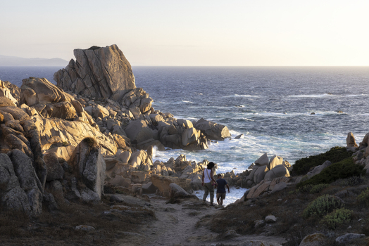 View of people walking on a path through the granite rock formations of Capo Testa towards the blue sea at sunset Capo Testa Sardegna Italy. View of people walking on a path through the granite rock formations of Capo Testa towards the blue sea at sunset Capo Testa Sardegna Italy.