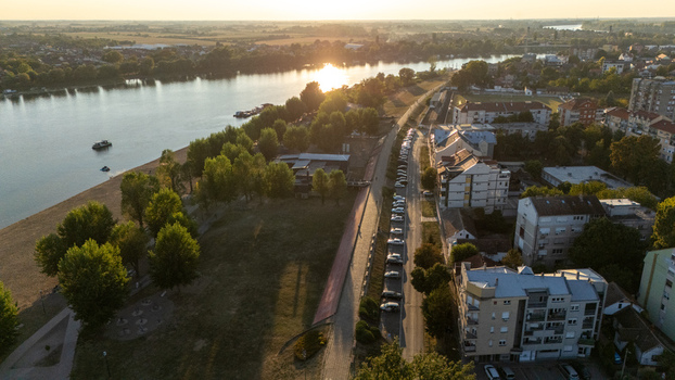 Aerial view of the Sava River riverside park road with parked cars and urban buildings bathed in golden hour light in Sremska Mitrovica Vojvodina Serbia. Aerial view of the Sava River riverside park road with parked cars and urban buildings bathed in golden hour light in Sremska Mitrovica Vojvodina Serbia.