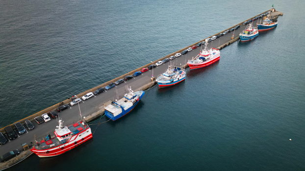 Aerial view of fishing boats moored along the pier their vibrant hulls contrasting with the dark sea Roscoff Brittany France.