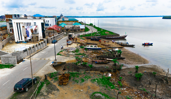 Aerial view of a coastal village with traditional wooden boats moored along the sandy shoreline modern buildings and a road running parallel to the water in Minima Rivers Nigeria.