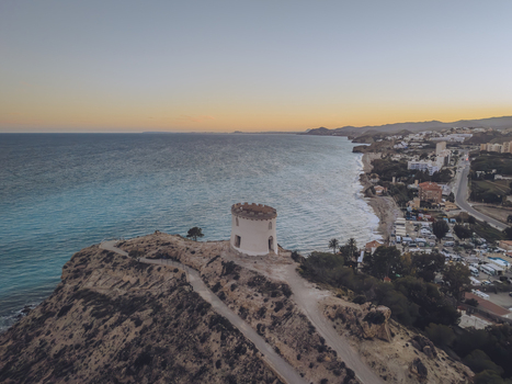 Aerial view of Santuari iber i roma de la Malladeta a white circular tower on a rocky cliff overlooking the turquoise Mediterranean Sea at sunset in La Vila Joiosa Comunidad Valenciana Spain. Aerial view of Santuari iber i roma de la Malladeta a white circular tower on a rocky cliff overlooking the turquoise Mediterranean Sea at sunset in La Vila Joiosa Comunidad Valenciana Spain.