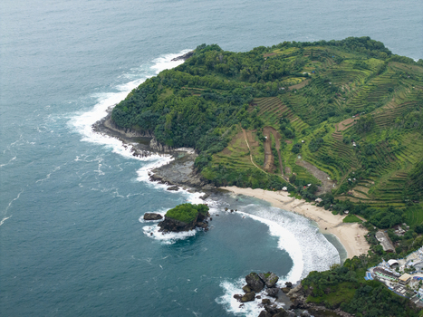 Aerial view of Jungwok Beach with lush green headlands golden sands deep blue ocean and white waves Gunungkidul Regency Special Region of Yogyakarta Indonesia. Aerial view of Jungwok Beach with lush green headlands golden sands deep blue ocean and white waves Gunungkidul Regency Special Region of Yogyakarta Indonesia.
