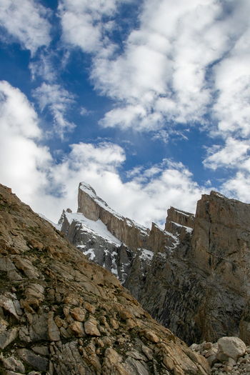 View of Trango Tower with snow capped peaks and rocky slopes under a blue sky with scattered clouds in Pakistan. View of Trango Tower with snow capped peaks and rocky slopes under a blue sky with scattered clouds in Pakistan.