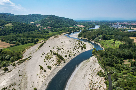 Aerial view of the Po River showing drought conditions with exposed gravel riverbeds and a narrow water channel surrounded by lush green vegetation and hills in Chivasso Piedmont Italy.