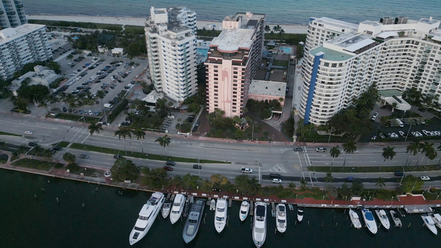 Aerial view of the Miami Beach waterfront featuring high rise residential buildings a busy coastal road and a marina filled with luxury yachts in Miami Beach Florida United States. Aerial view of the Miami Beach waterfront featuring high rise residential buildings a busy coastal road and a marina filled with luxury yachts in Miami Beach Florida United States.