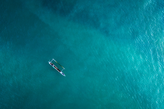 Aerial view of a traditional wooden boat floating on the turquoise ocean water with slight ripples at Tanjung Aan Beach Kecamatan Pujut Nusa Tenggara Barat Indonesia.