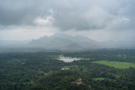View of the lush tropical landscape with a small lake and misty mountains under an overcast sky in Sigiriya Central Province Sri Lanka. View of the lush tropical landscape with a small lake and misty mountains under an overcast sky in Sigiriya Central Province Sri Lanka.