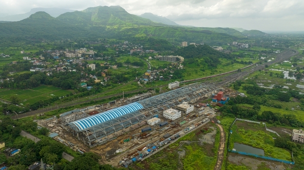 Aerial view of the Karjat railway station construction site with a large blue and white arched roof surrounded by lush green landscape and railway tracks in Karjat Maharashtra India.