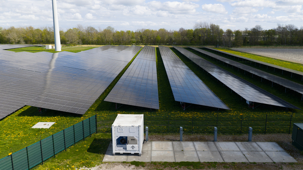 Aerial view of rows of solar panels in a large solar farm with a wind turbine and green fields under a cloudy sky in Warmenhuizen North Holland Netherlands. Aerial view of rows of solar panels in a large solar farm with a wind turbine and green fields under a cloudy sky in Warmenhuizen North Holland Netherlands.