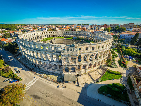 Aerial view of the ancient Roman amphitheater a colossal stone structure bathed in warm sunlight stands as a testament to history against the azure sky Pula Istria County Croatia.