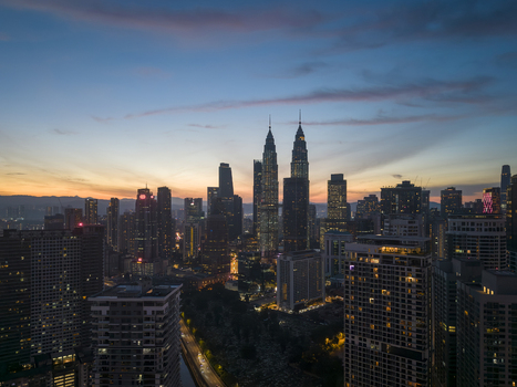 Kuala Lumpur Malaysia 11 March 2026 Aerial view of the Petronas Twin Towers and the city skyline at sunset with glowing building lights and a colorful twilight sky.