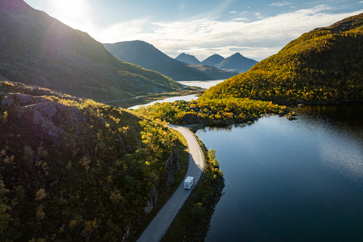 Aerial view of a camper van driving along a scenic coastal road surrounded by mountains and autumn foliage near a lake in Kvaloya Troms Norway.