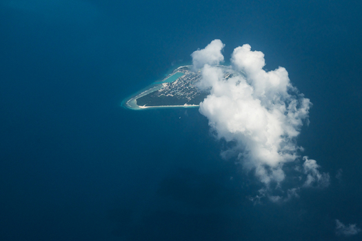 Aerial view of a small island with white sandy beaches fringed by turquoise waters and a cluster of fluffy white clouds Flight from Male to Hanimaadhoo island Maldives.