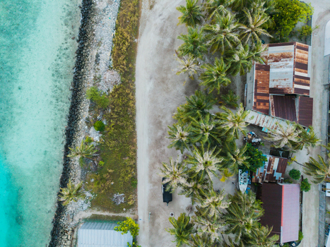 Aerial view of the coastline where turquoise waters meet the sandy shore lined with verdant palm trees and rustic buildings Vashafaru Island Maldives. Aerial view of the coastline where turquoise waters meet the sandy shore lined with verdant palm trees and rustic buildings Vashafaru Island Maldives.
