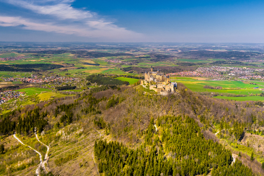 Hechingen Baden Wurttemberg Germany 27 September 2026 Aerial view of Hohenzollern Castle perched on a hilltop surrounded by dense forests and rolling green fields under a clear blue sky.