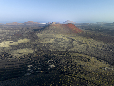Aerial view of the volcanic landscape of Lanzarote with its iconic red volcanic cones vast lava fields and traditional circular vineyard pits in Lanzarote Canarias Spain. Aerial view of the volcanic landscape of Lanzarote with its iconic red volcanic cones vast lava fields and traditional circular vineyard pits in Lanzarote Canarias Spain.