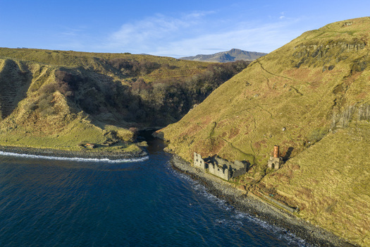 Aerial view of the historic ruins at Lealt Falls along the rugged coastline with steep grassy cliffs and blue sea Isle of Skye Scotland United Kingdom. Aerial view of the historic ruins at Lealt Falls along the rugged coastline with steep grassy cliffs and blue sea Isle of Skye Scotland United Kingdom.