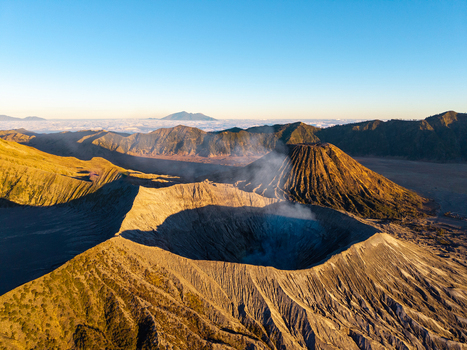 Aerial view of Mount Bromo with its smoking volcanic crater and rugged landscape illuminated by golden hour light in Tosari East Java Indonesia.