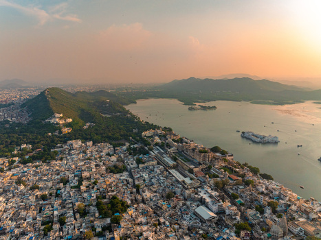 Aerial view of the historic city of Udaipur with the City Palace complex on the banks of Lake Pichola surrounded by hills and urban rooftops at sunset in Udaipur Rajasthan India. Aerial view of the historic city of Udaipur with the City Palace complex on the banks of Lake Pichola surrounded by hills and urban rooftops at sunset in Udaipur Rajasthan India.