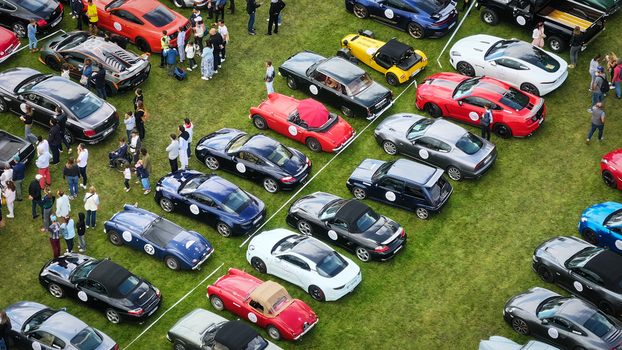 La Chapelle de Guinchay France 01 June 2024 Aerial view of classic and modern sports cars parked on a green lawn with people walking around during an outdoor automotive event.