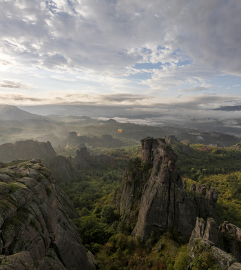 Aerial view of the Belogradchik Rocks with unique sandstone formations lush green forests and a hot air balloon floating in the distance in Belogradchik Vidin Bulgaria.