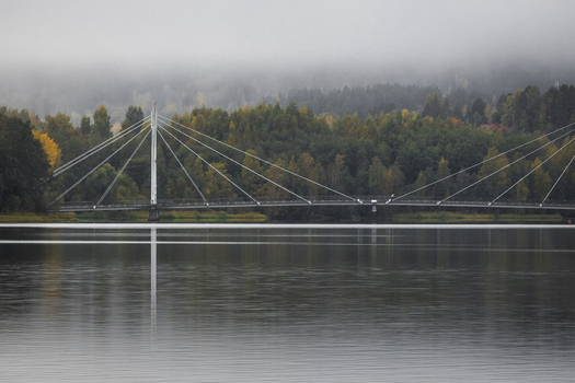 View of the Ylistonrinne Bridge spanning across the calm waters of Lake Jyvasjarvi with autumn foliage and a misty sky in the background in Jyvaskyla Central Finland Finland.