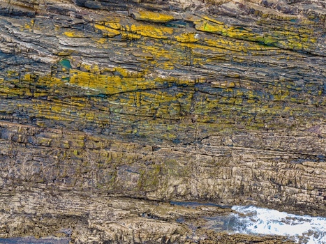 Aerial view of the textured rock formations and vibrant yellow lichen on the cliffs at Silence Beach Viewpoint Cudillero Asturias Spain.