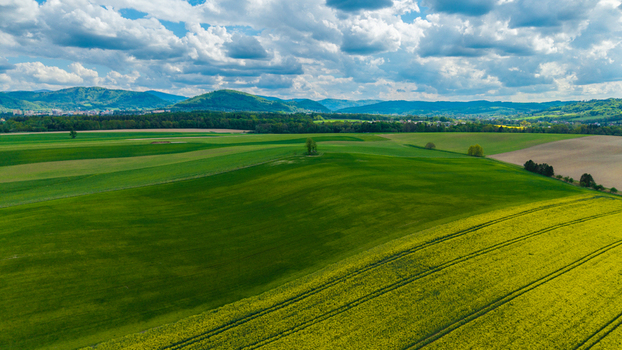 Aerial view of rolling green hills and vibrant yellow rapeseed fields under a cloudy sky with mountains in the background Pribor Moravian Silesian Region Czechia. Aerial view of rolling green hills and vibrant yellow rapeseed fields under a cloudy sky with mountains in the background Pribor Moravian Silesian Region Czechia.