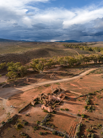 Aerial view of the historic Kanyaka Station ruins surrounded by red earth dirt tracks and sparse vegetation under a dramatic cloudy sky in Flinders Ranges South Australia Australia. Aerial view of the historic Kanyaka Station ruins surrounded by red earth dirt tracks and sparse vegetation under a dramatic cloudy sky in Flinders Ranges South Australia Australia.