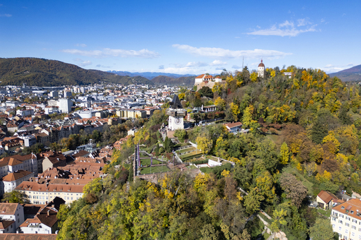 Aerial view of the Schlossberg hill crowned with the iconic clock tower overlooking the old town s terracotta rooftops and the distant hazy mountains Graz Styria Austria.