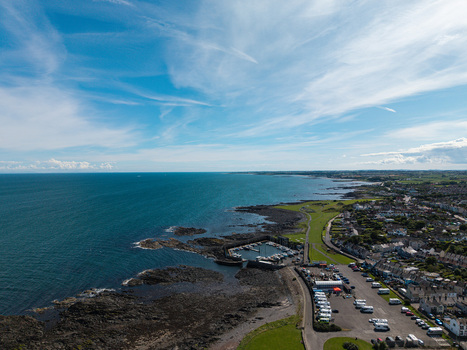 Aerial view of Donaghadee Harbour with boats docked in the basin surrounded by rocky coastline green fields and the town of Donaghadee Northern Ireland United Kingdom. Aerial view of Donaghadee Harbour with boats docked in the basin surrounded by rocky coastline green fields and the town of Donaghadee Northern Ireland United Kingdom.