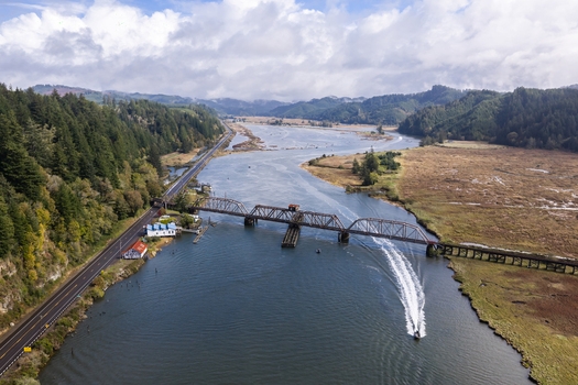 Aerial view of the Siuslaw River Train Bridge near Florence Oregon with salmon fishing boats coastal wetlands forest and transportation routes along the estuary.
