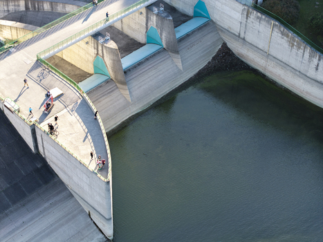 Aerial view of Niedzica Dam with people walking along the concrete structure and green railings overlooking the water reservoir in Niedzica Malopolskie Poland.